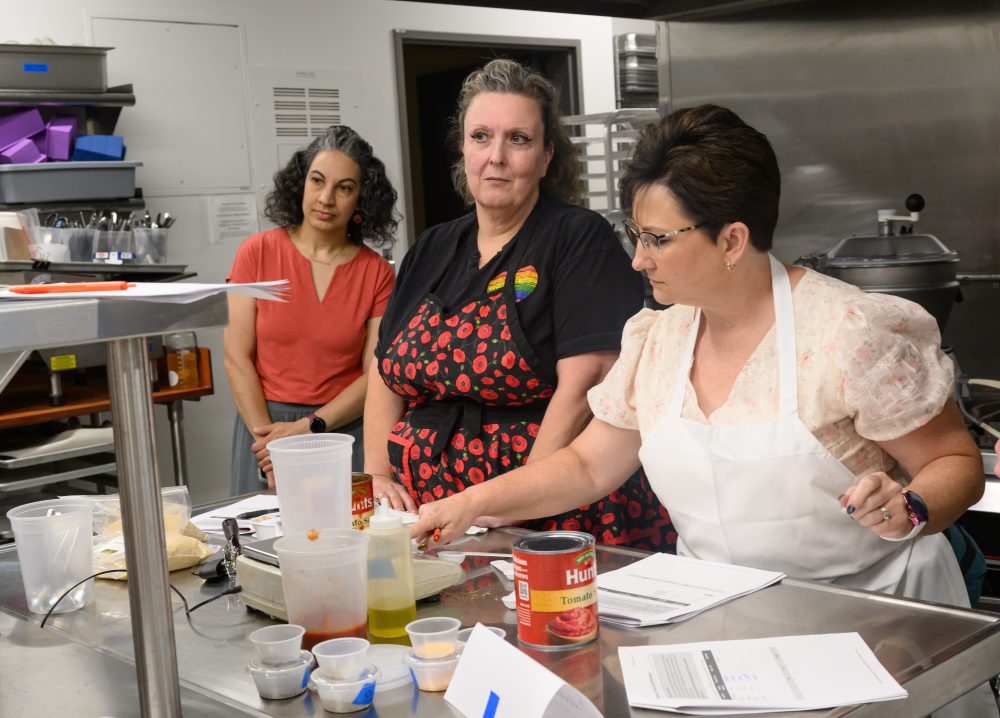 Katrina Stein observes Hillsboro School District culinary arts and hospitality instructors Melissa Buechler and Kristi Moe at the PCC CTE Summit in a commercial kitchen.