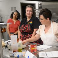 Katrina Stein observes Hillsboro School District culinary arts and hospitality instructors Melissa Buechler and Kristi Moe at the PCC CTE Summit in a commercial kitchen.