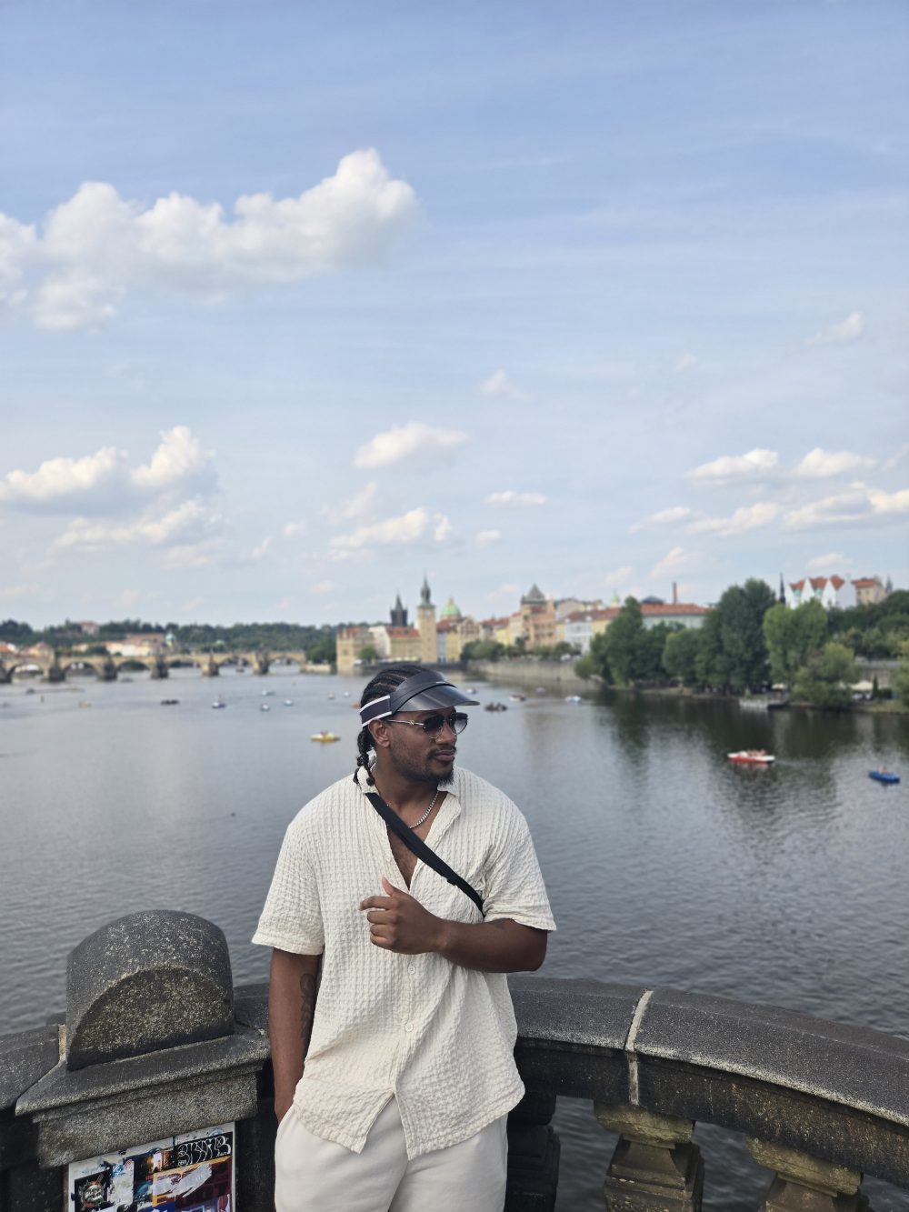 Young man stands before Czech city of Prague at riverbank.