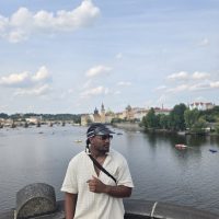 Young man stands before Czech city of Prague at riverbank.