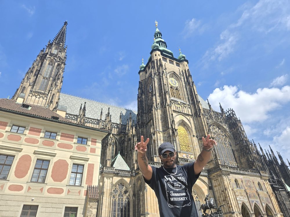Young Black man with hands held high before historic center.