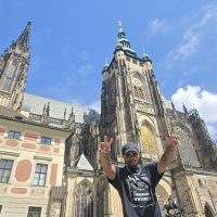 Young Black man with hands held high before historic center.