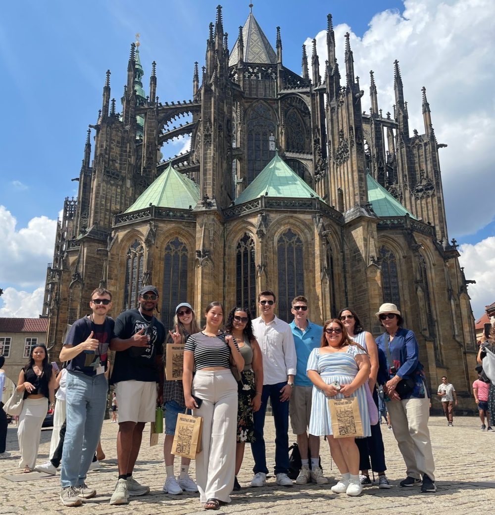 A dozen study abroad students stand before a astle of antiquity in Prague dressed casually..