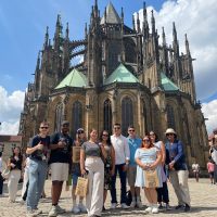 A dozen study abroad students stand before a astle of antiquity in Prague dressed casually..