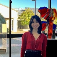 Smiling young woman stands before a sculputral gallery piece in red glass.
