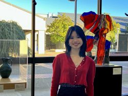 Smiling young woman stands before a sculputral gallery piece in red glass.