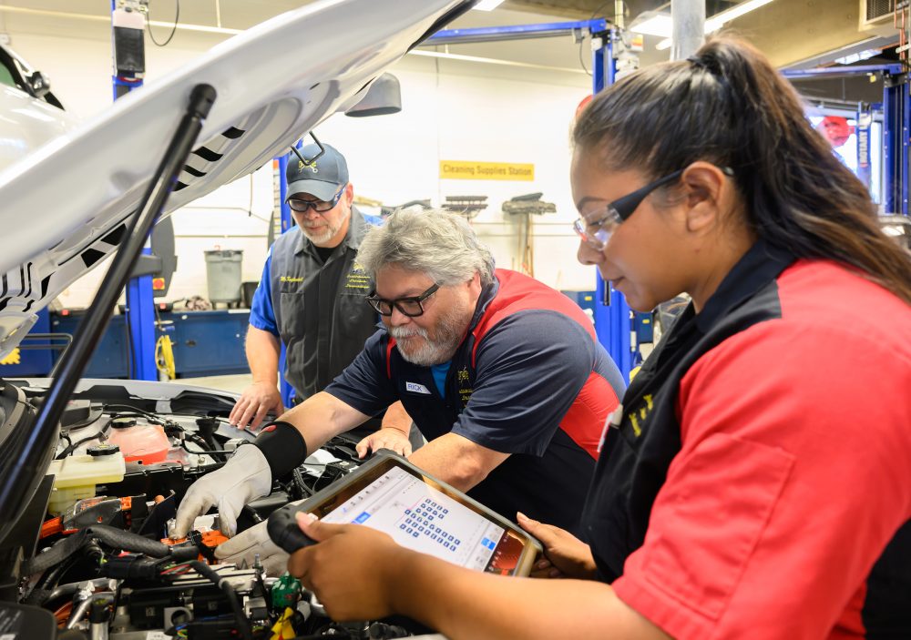 Rick Cruz works on PCC's new EV training vehicle as fellow alum monitors the system as automotive service instructor Jay Kuykendall oversees their work.
