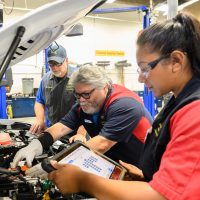 Rick Cruz works on PCC's new EV training vehicle as fellow alum monitors the system as automotive service instructor Jay Kuykendall oversees their work.