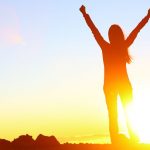 A woman with her arms up in victory after having reached the summit.