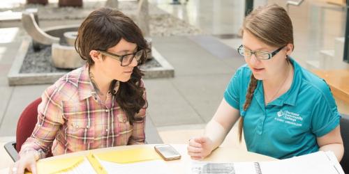Two females sitting on a table reviewing a paper
