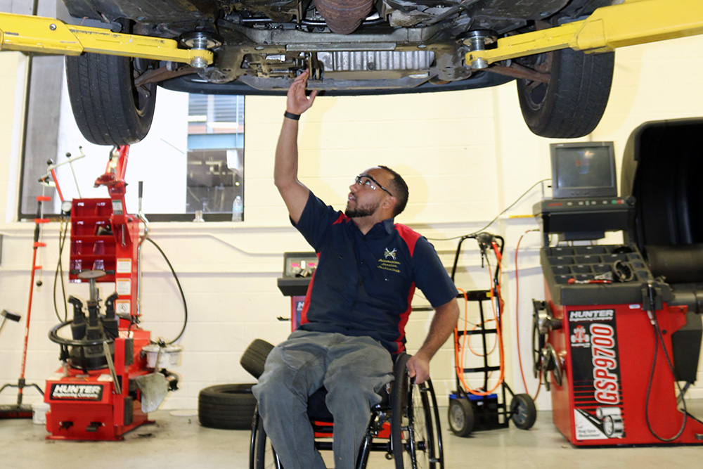 Automotive Service student in a wheelchair working below a raised car