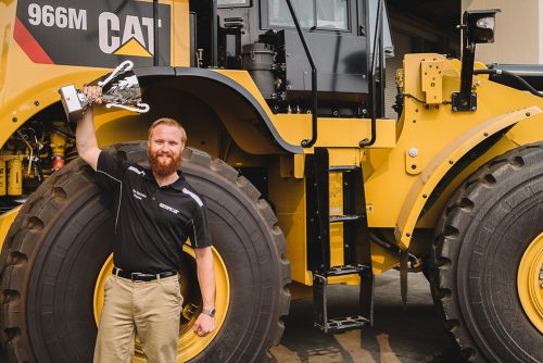 Ryan Walker holding his prize in front of a Caterpillar