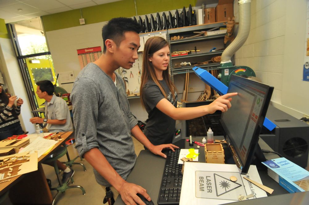 two students helping each other at a large computer display