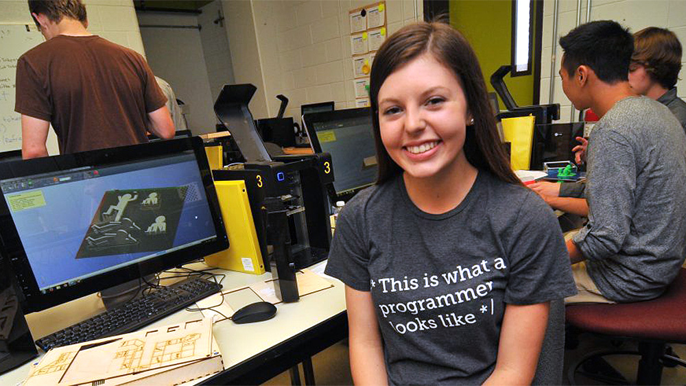 young woman at a computer with a shirt that says this is what a programmer looks like