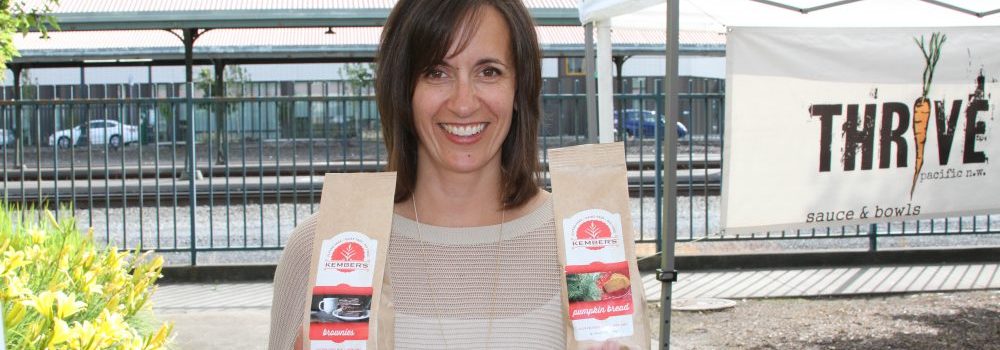 Marilyn Kember, owner at Kember’s Gluten Free, smiles while holding up two bags of her baked goods recipe mixes, one in each hand
