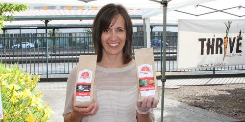 Marilyn Kember, owner at Kember’s Gluten Free, smiles while holding up two bags of her baked goods recipe mixes, one in each hand