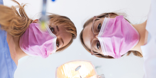 two dental assistants peering at a patient with tools in hand