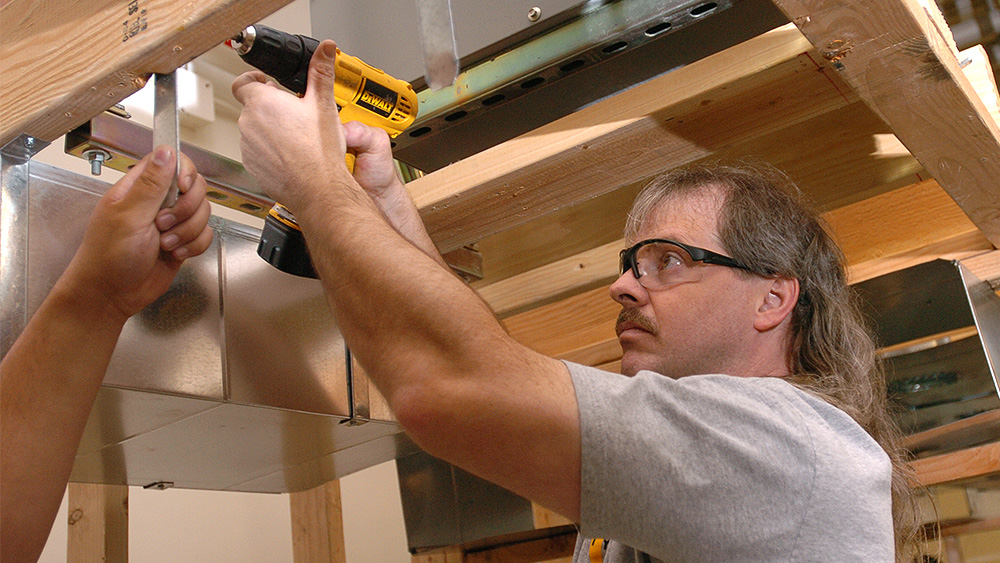 Student using a power drill on a wall frame