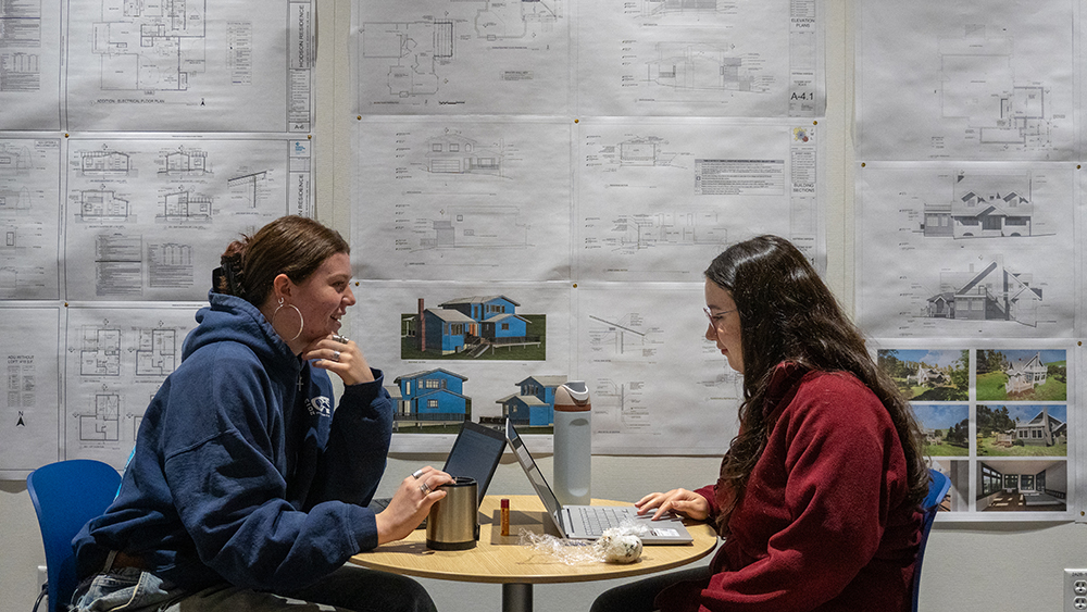 Two students sitting in front of architectural drawings