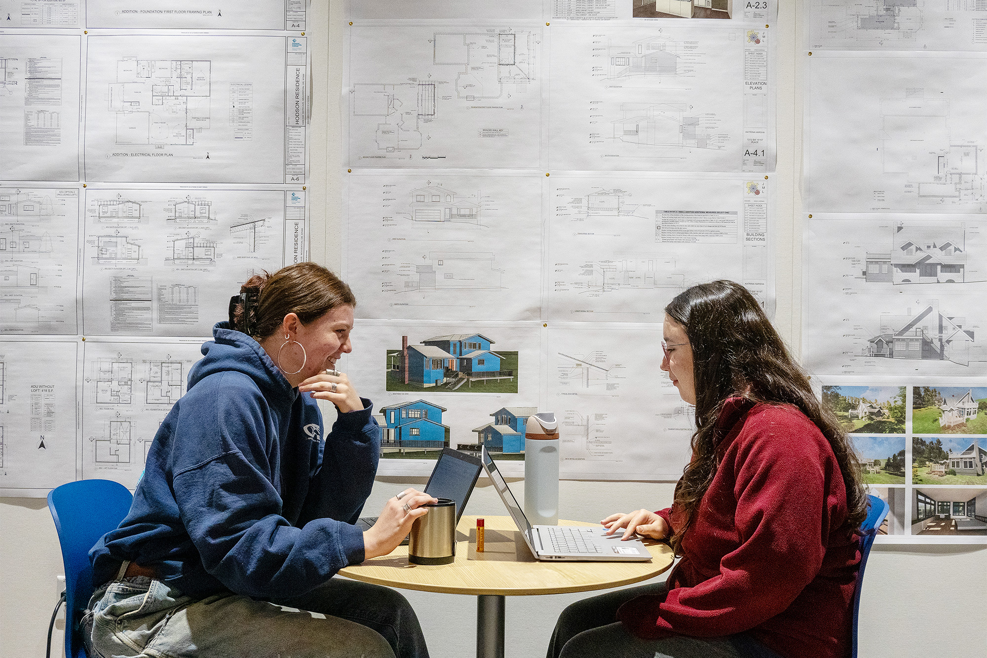 Architectural Design and Drafting students studying together in front of a wall of printed house plans