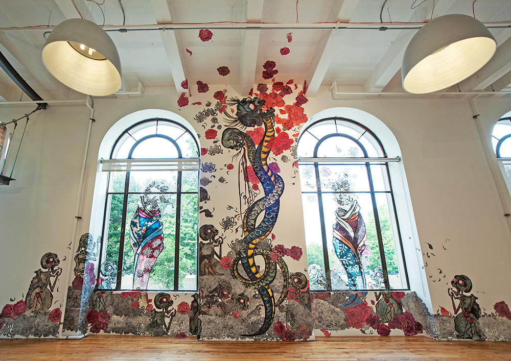 Large colorful mural up a wall between two large windows showing figures and abstract snake imagery