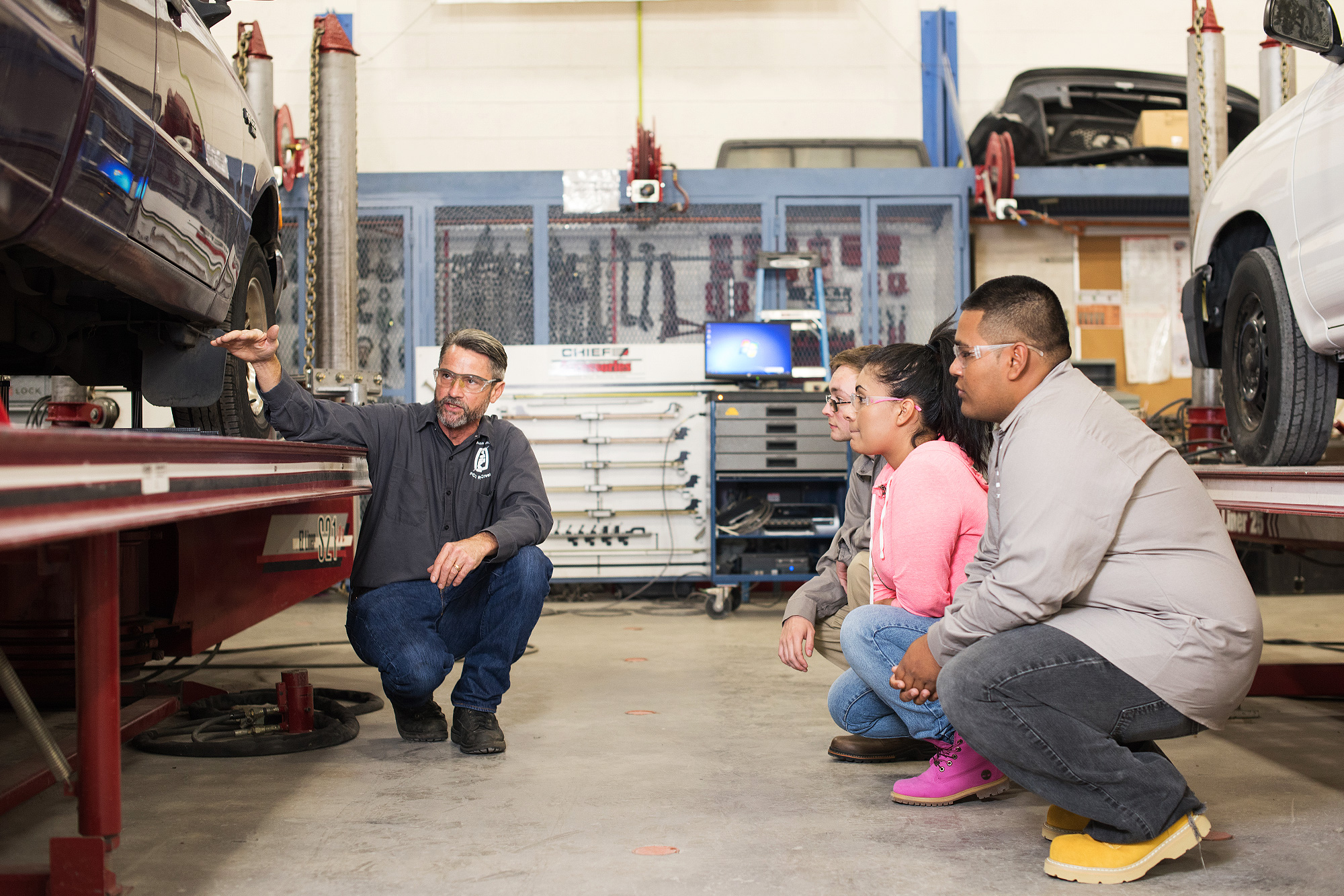 Instructor and students squatting by a car and discussing the car's body