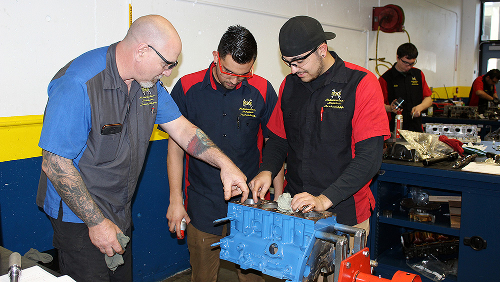 Students looking at a piece of engine with an instructor in the shop