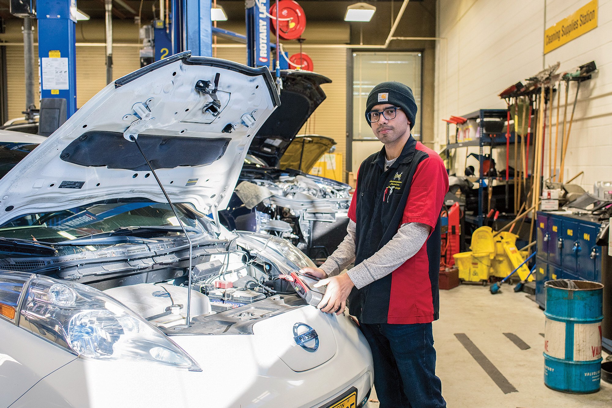 Auto Service student standing next to an electric vehicle with the hood open