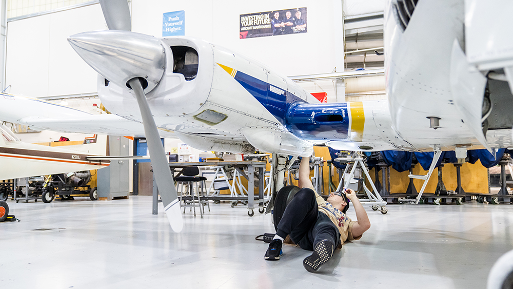 Student working on the underside of an airplane