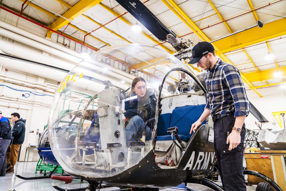 Students sitting in and working on a helicopter in the hangar