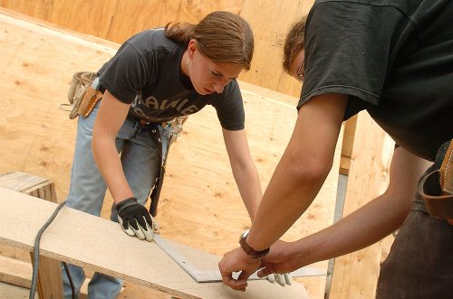 Female student measuring a piece of wood at a job site