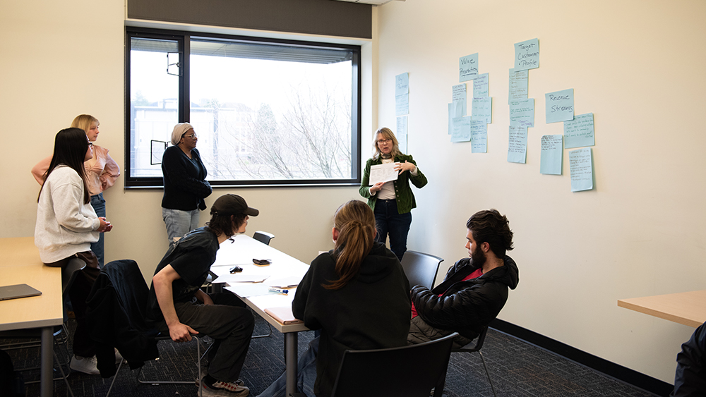 Instructor teaching students with business-related topics taped to the wall behind her