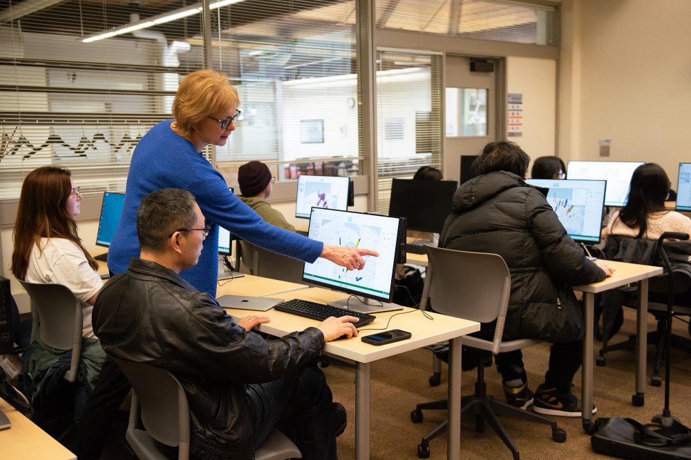 Instructor pointing at a students computer and explaining a concept in class