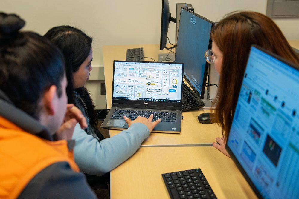 Students looking at a laptop together that shows Excel marketing dashboard templates