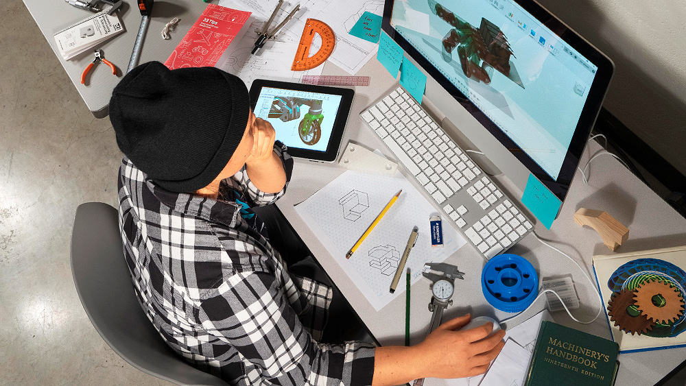 CADD student working on a computer surrounded by tools of the trade at her workstation