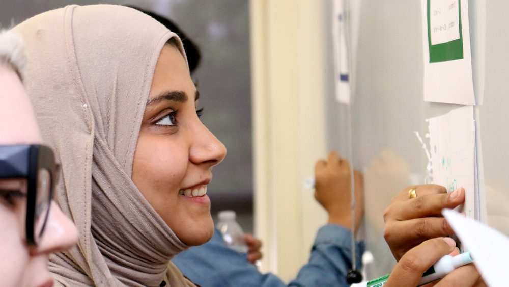 Student in hijab doing math on white board