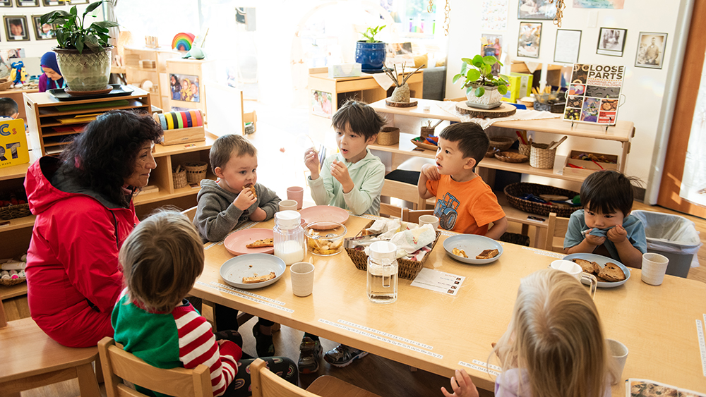 Young students eating snack in a classroom with their teacher