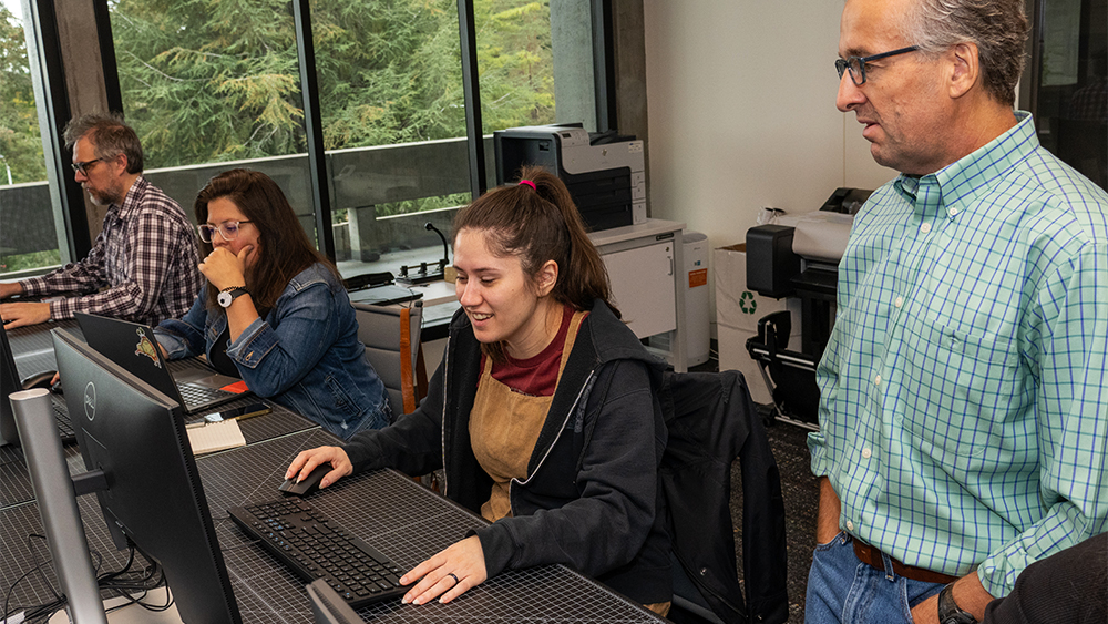 Student working at a computer in class while her instructor assists