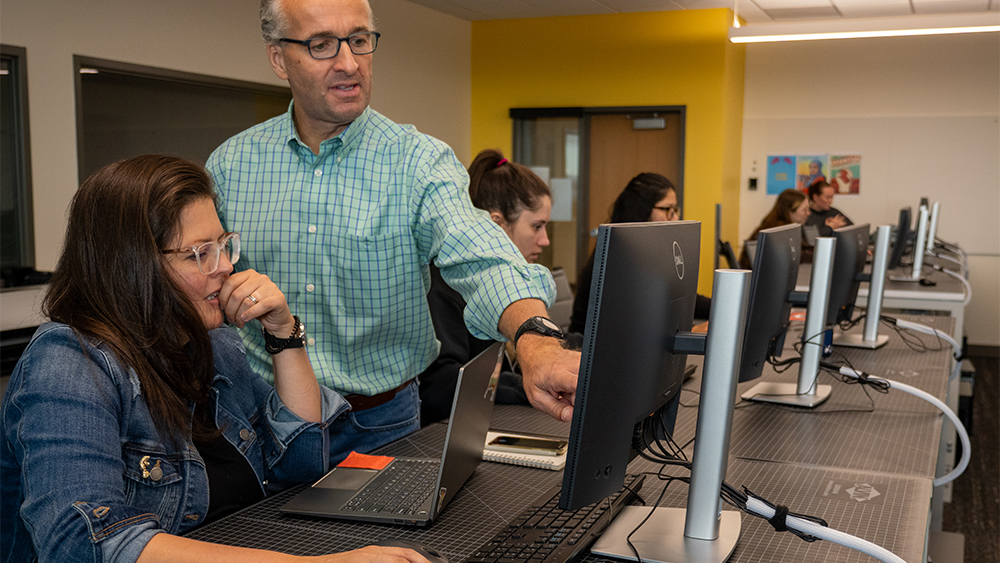 Student assisting a student at a computer in class