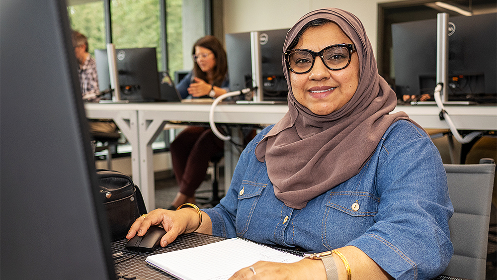 Student smiling at the camera while working on a computer in class