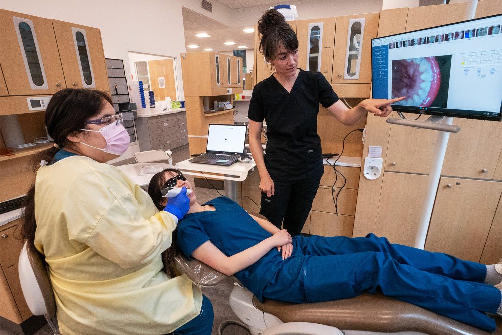 Dental assisting student learning how to use a camera to look at teeth with an instructor