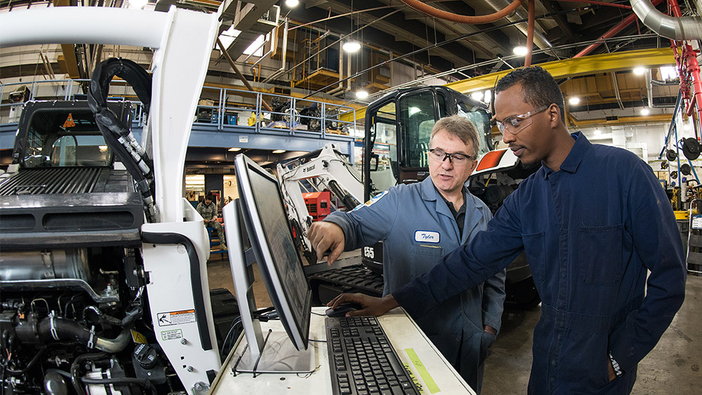 Student and instructor standing at a computer in the diesel shop, with diesel engines and equipment all around them