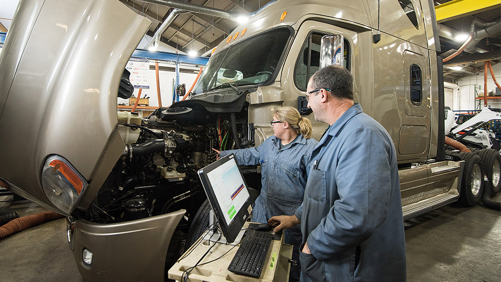 Student and instructor examining a semi truck engine in the shop