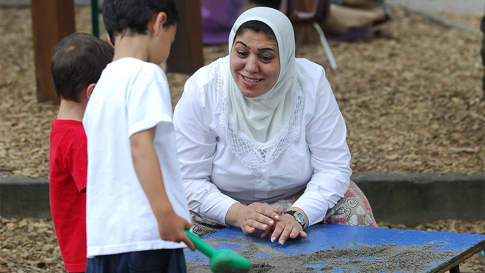 Adult playing with two children in a sandbox at a playground