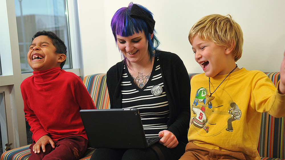 Student working with two children on a laptop, all three are laughing