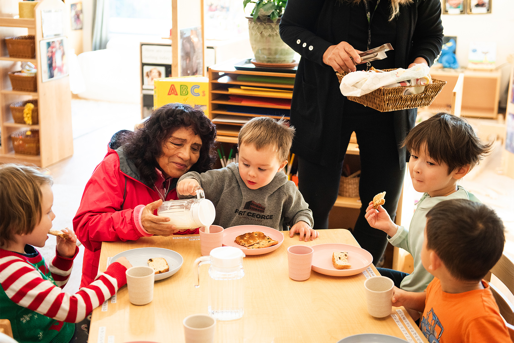 Aide helping a child pour milk at lunch in the Childcare Development Center