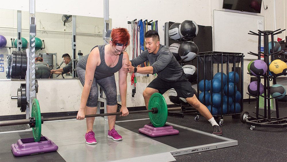 Student working with a personal trainer lifting weights