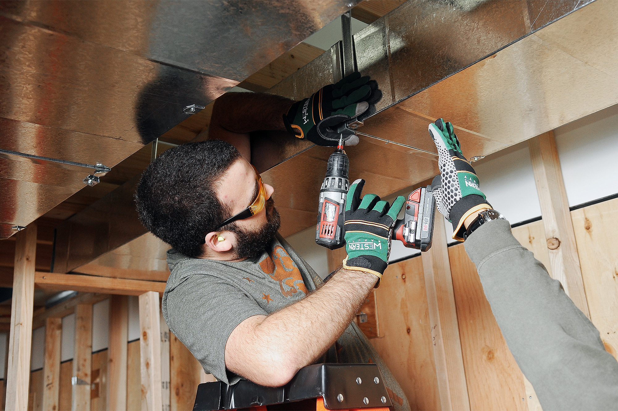 Facilities Maintenance installing ducting into a ceiling