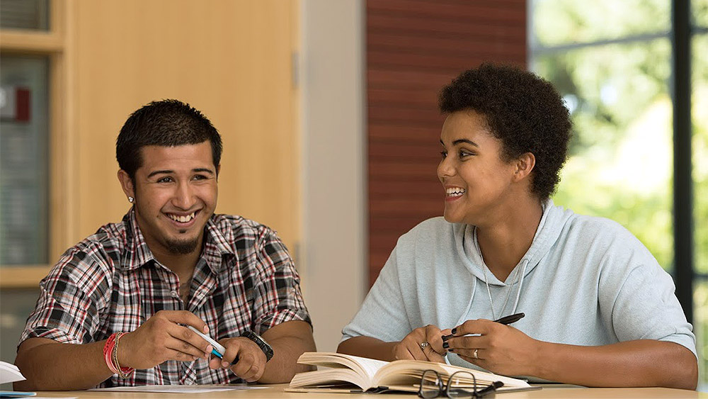 Students working with a novel and a notebook laughing together