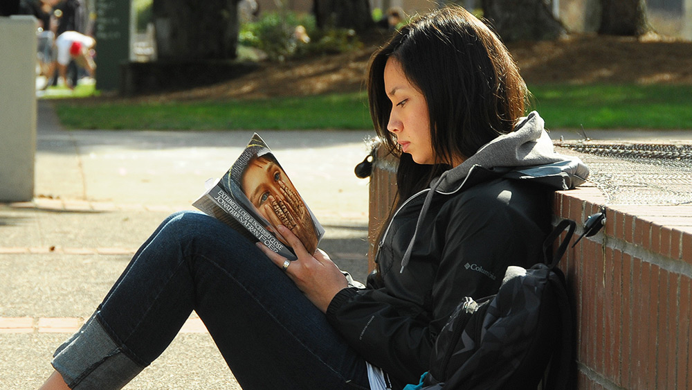 Student reading a book called Exremely Loud and Incredibly Close outside on campus